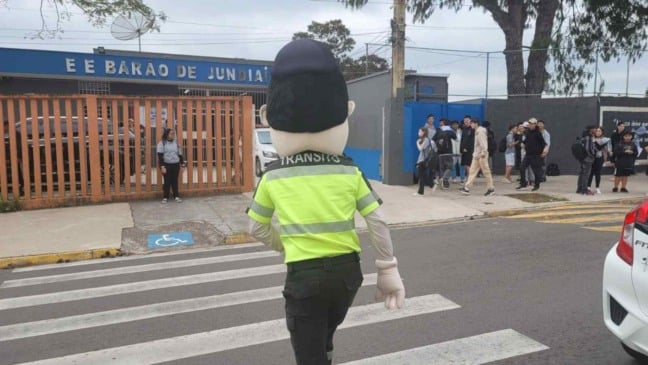 Mascote de trânsito atravessa faixa de pedestres em frente à Escola Barão de Jundiaí durante ação educativa da Semana Nacional do Trânsito.
