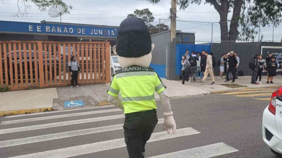 Mascote de trânsito atravessa faixa de pedestres em frente à Escola Barão de Jundiaí durante ação educativa da Semana Nacional do Trânsito.
