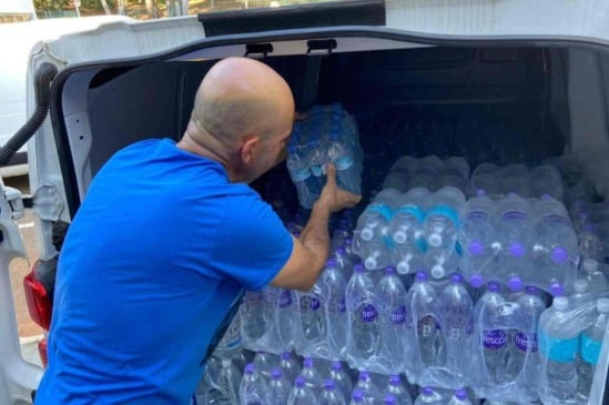 Homem em camisa azul carrega água mineral em veículo para arrecadação de doações às vítimas das chuvas.