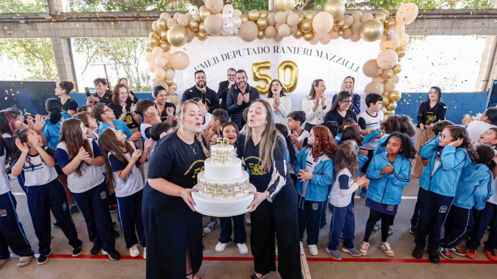 Diretoras da EMEB Ranieri Mazzilli cortam bolo com alunos celebrando os 50 anos da escola.