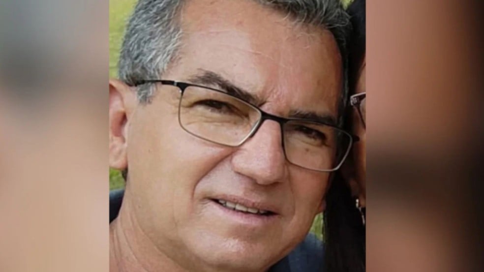 Homem de cabelos grisalhos e óculos de armação preta em close-up, olhando para a câmera.