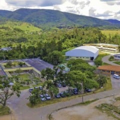 Vista aérea do campus da Etec Benedito Storani, em Jundiaí, cercado por áreas verdes e montanhas ao fundo. A imagem mostra os prédios da escola, ginásio, estacionamentos e áreas de convivência, destacando a integração da instituição com o ambiente natural.