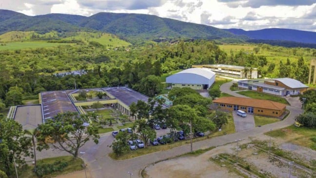 Vista aérea do campus da Etec Benedito Storani, em Jundiaí, cercado por áreas verdes e montanhas ao fundo. A imagem mostra os prédios da escola, ginásio, estacionamentos e áreas de convivência, destacando a integração da instituição com o ambiente natural. Vista aérea do campus da Etec Benedito Storani, em Jundiaí, cercado por áreas verdes e montanhas ao fundo. A imagem mostra os prédios da escola, ginásio, estacionamentos e áreas de convivência, destacando a integração da instituição com o ambiente natural.