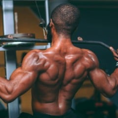 Homem fazendo exerc&iacute;cio de costas em aparelho na academia