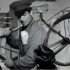 Cena do filme Ladrões de Bicicletas mostra homem segurando bicicleta e conversando com um garoto, em ambiente simples e em preto e branco.