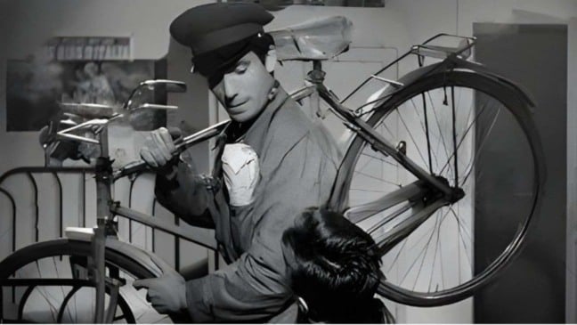 Cena do filme Ladrões de Bicicletas mostra homem segurando bicicleta e conversando com um garoto, em ambiente simples e em preto e branco.