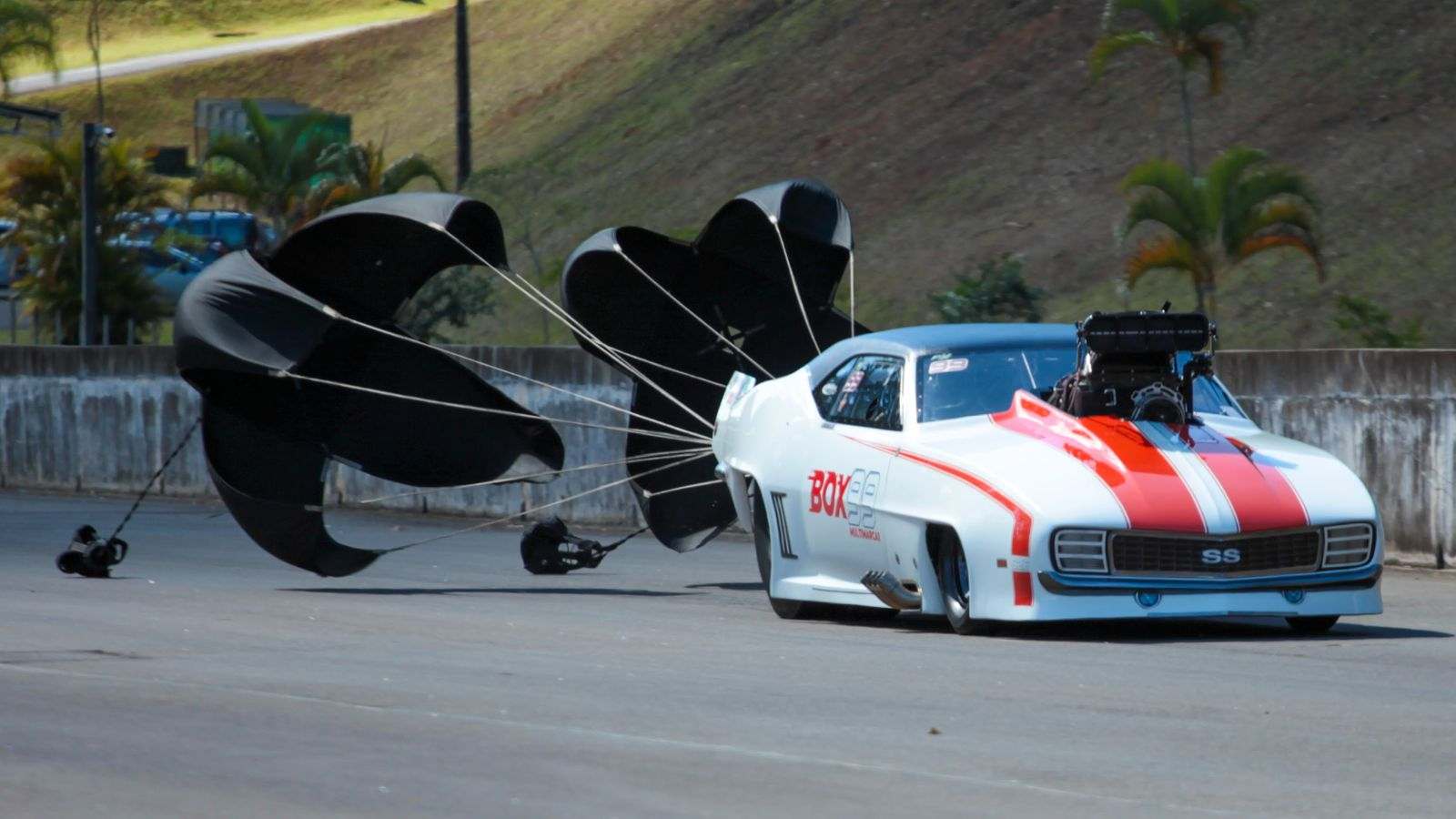 Carro de arrancada ProMod branco com listras vermelhas usando paraquedas de frenagem na pista da SPID, em Itatiba.