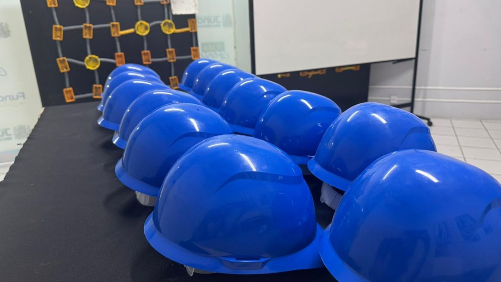 Vários capacetes azuis dispostos em fila sobre uma mesa, em sala de treinamento do Fundo Social de Jundiaí.