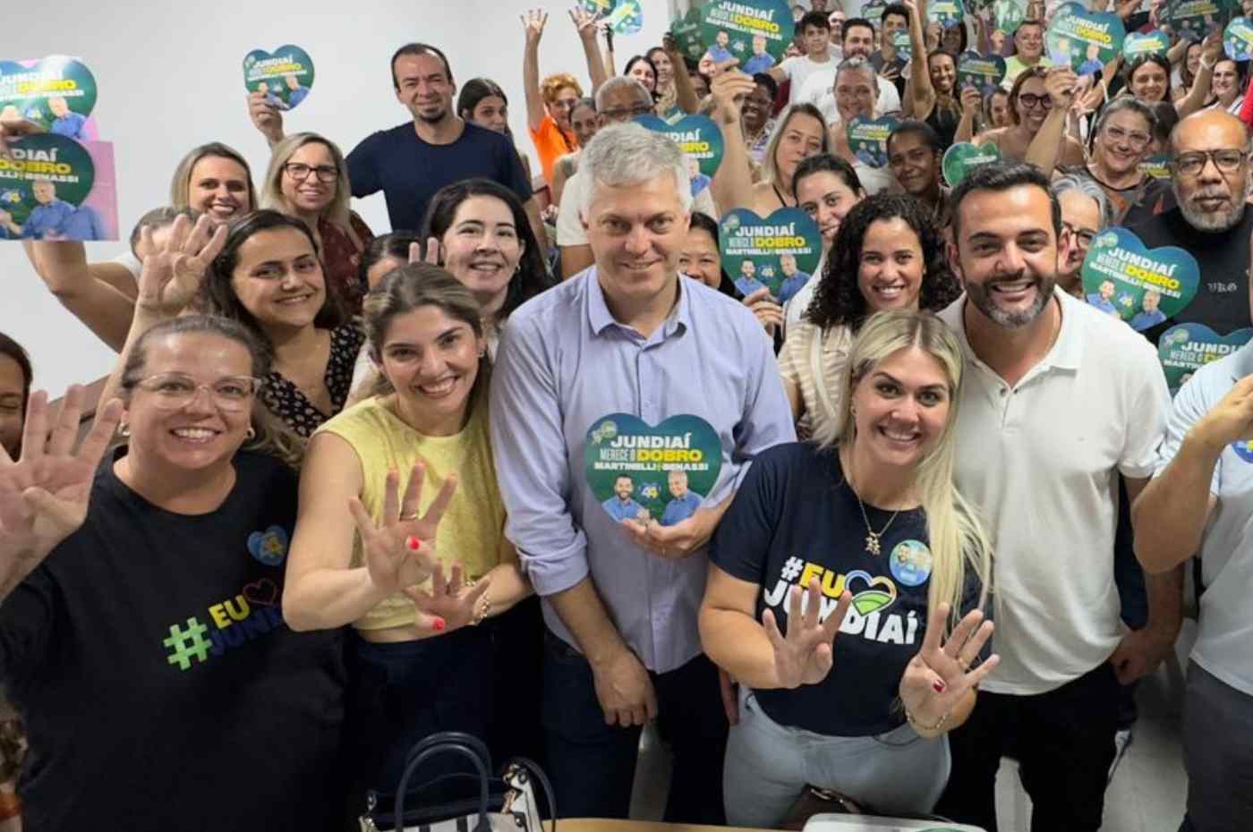 Grupo de educadores e Gustavo Martinelli em reunião de campanha, segurando placas com o slogan 
