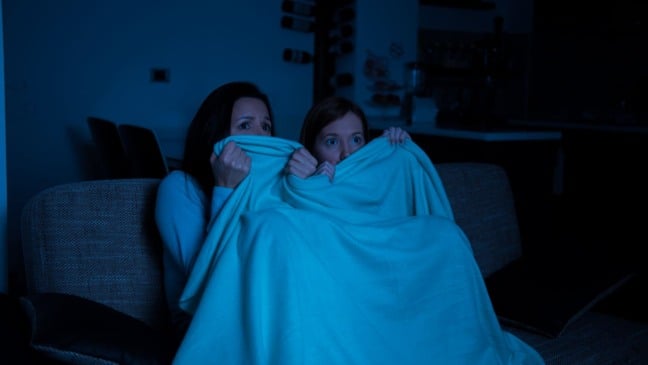 Duas mulheres com olhar assustado assistem a um filme de terror cobertas por um cobertor azul. Duas mulheres com olhar assustado assistem a um filme de terror cobertas por um cobertor azul.