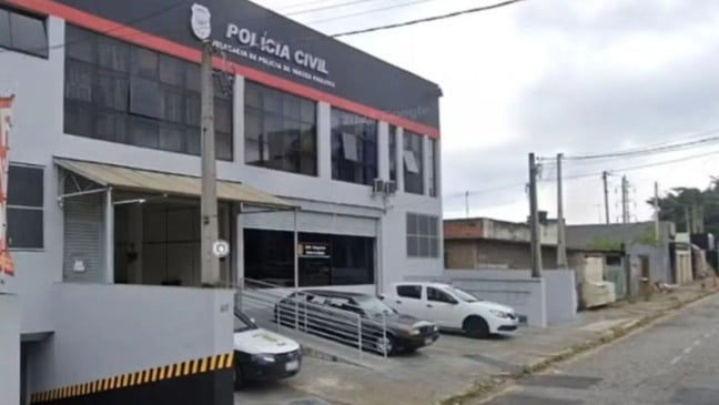 Fachada da Delegacia de Polícia Civil de Várzea Paulista com viaturas estacionadas na entrada e céu nublado ao fundo.