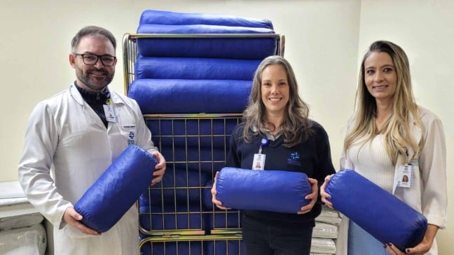 Equipe do Hospital São Vicente de Jundiaí segura coxins azuis feitos com uniformes reciclados em ação sustentável.