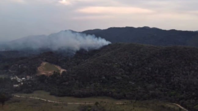 Vista aérea da Serra do Japi com fumaça subindo da vegetação devido a um incêndio florestal em Jundiaí, São Paulo.