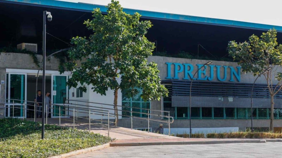 Fachada do prédio do IPREJUN em Jundiaí, com letreiro azul e entrada acessível com rampa cercada por árvores. Fachada do prédio do IPREJUN em Jundiaí, com letreiro azul e entrada acessível com rampa cercada por árvores.