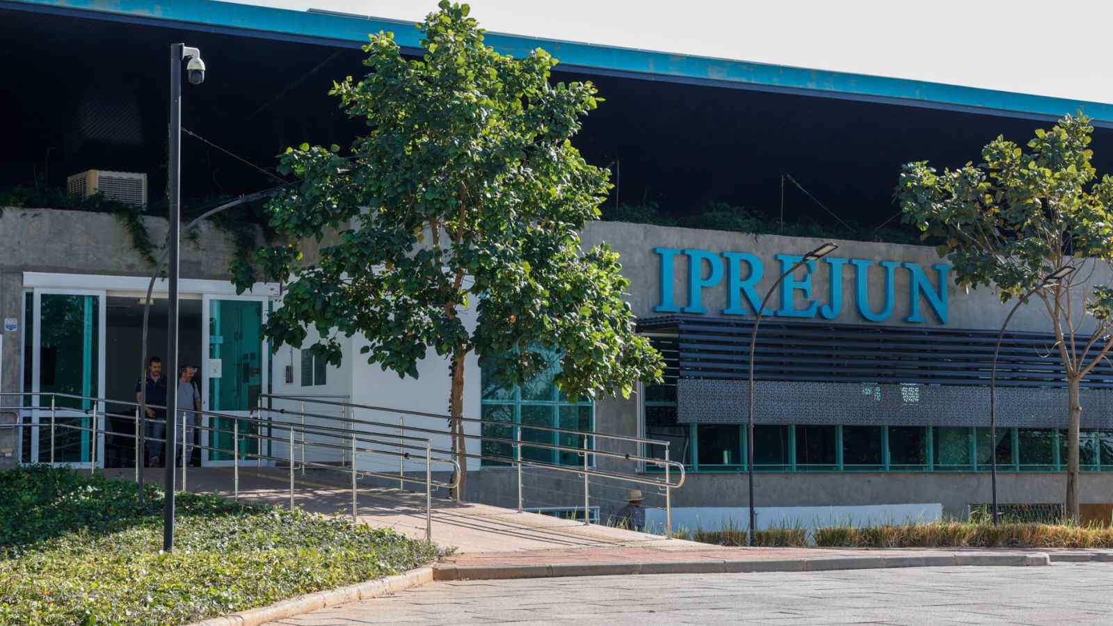 Fachada do prédio do IPREJUN em Jundiaí, com letreiro azul e entrada acessível com rampa cercada por árvores.