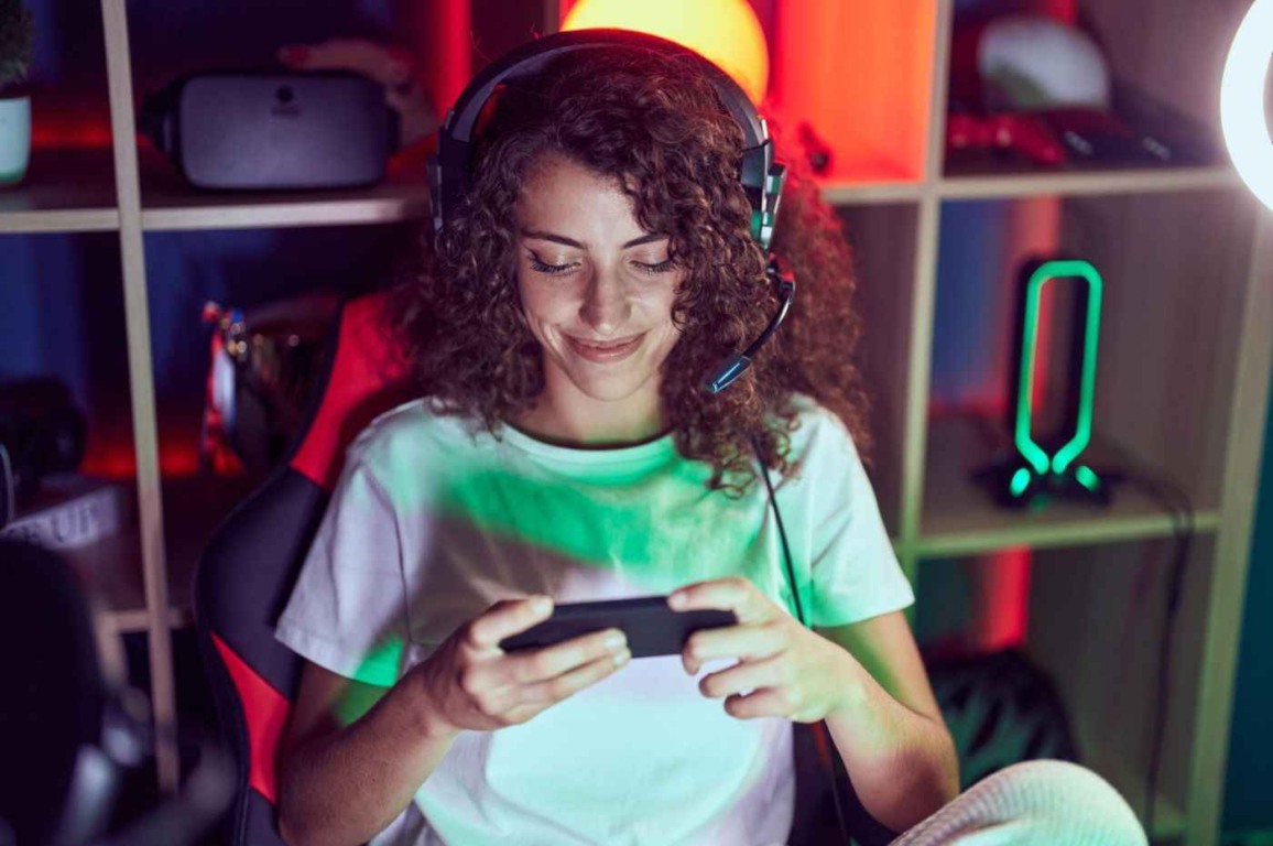 Mulher sorrindo jogando em cassino online no celular, com fones de ouvido e ambiente iluminado, refletindo a atmosfera de jogos. Mulher sorrindo jogando em cassino online no celular, com fones de ouvido e ambiente iluminado, refletindo a atmosfera de jogos.