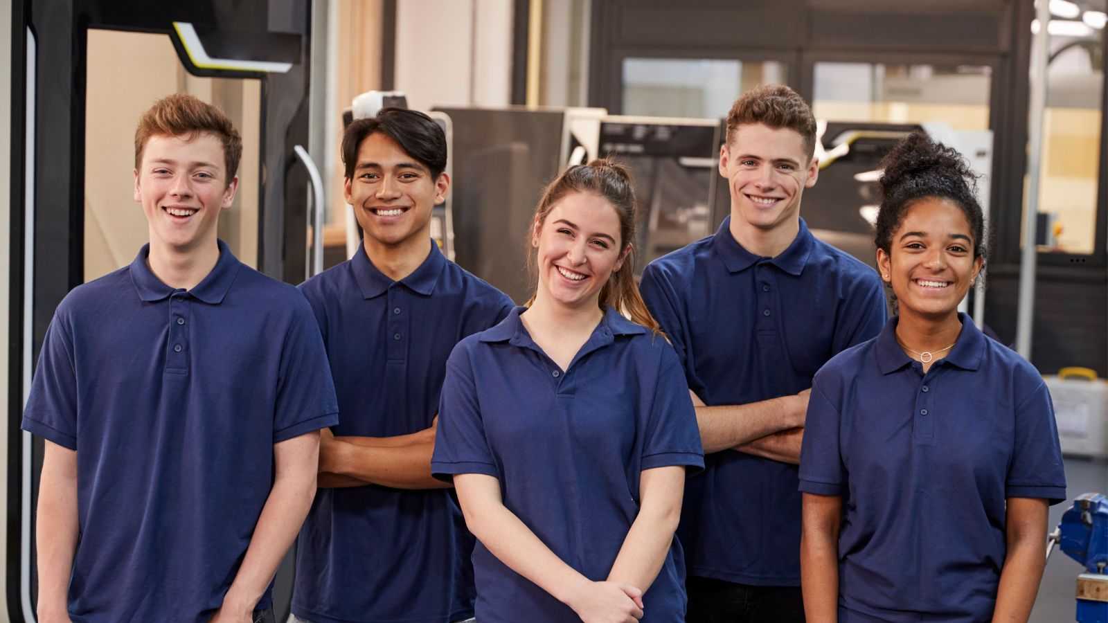 Cinco jovens aprendizes uniformizados com camisetas azul-marinho sorrindo em ambiente de trabalho, simbolizando estágio e programas de capacitação profissional.