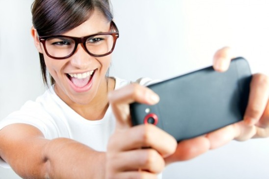Mulher sorridente com óculos tirando selfie no celular, simbolizando diversão e interação com os melhores jogos de celular.