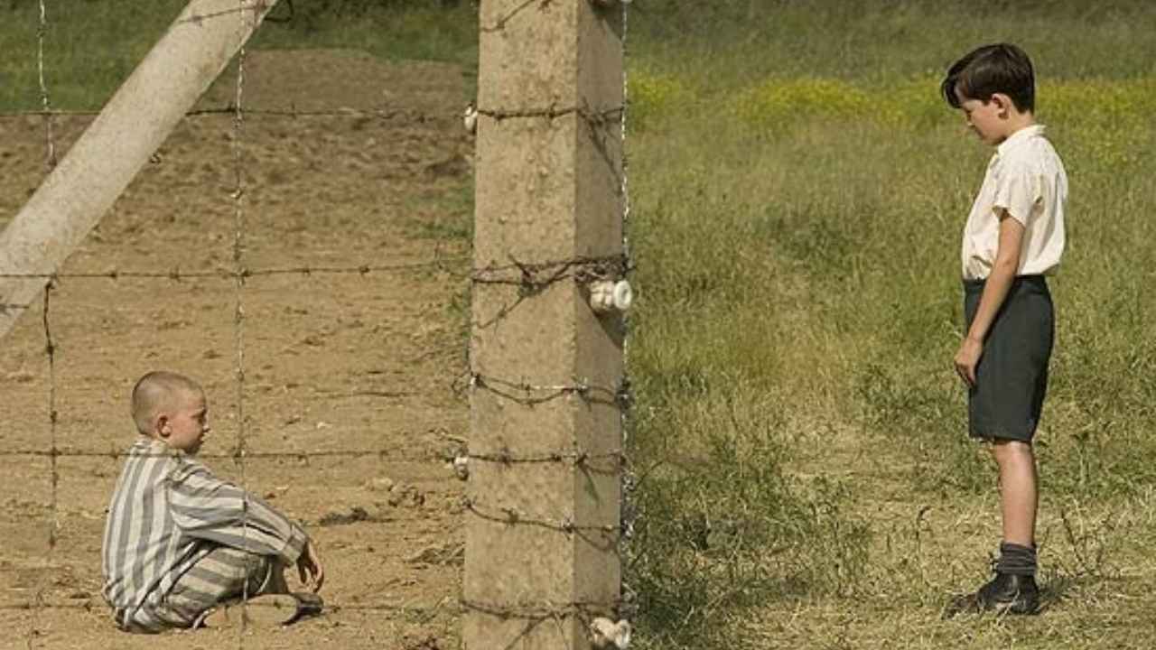 Cena de filme nos lançamentos da Netflix, dois meninos separados por cerca de arame, um sentado e outro em pé.