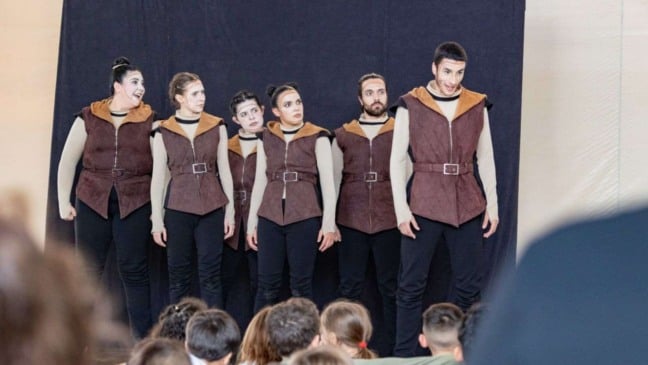 Atores da Companhia de Teatro de Jundiaí encenam o espetáculo “Robin Hood” diante de crianças, usando figurinos medievais marrom e bege e maquiagem teatral.