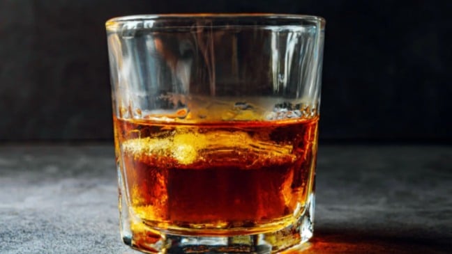 Copo com bebida de cor âmbar e gelo sobre mesa escura, ilustrando o consumo de bebidas alcoólicas.