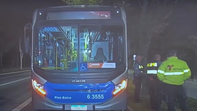 Ônibus da linha 6000/10 parado em via de Parelheiros, em São Paulo, com agentes da SPTrans e policiais ao lado durante abordagem após crime cometido pelo motorista.