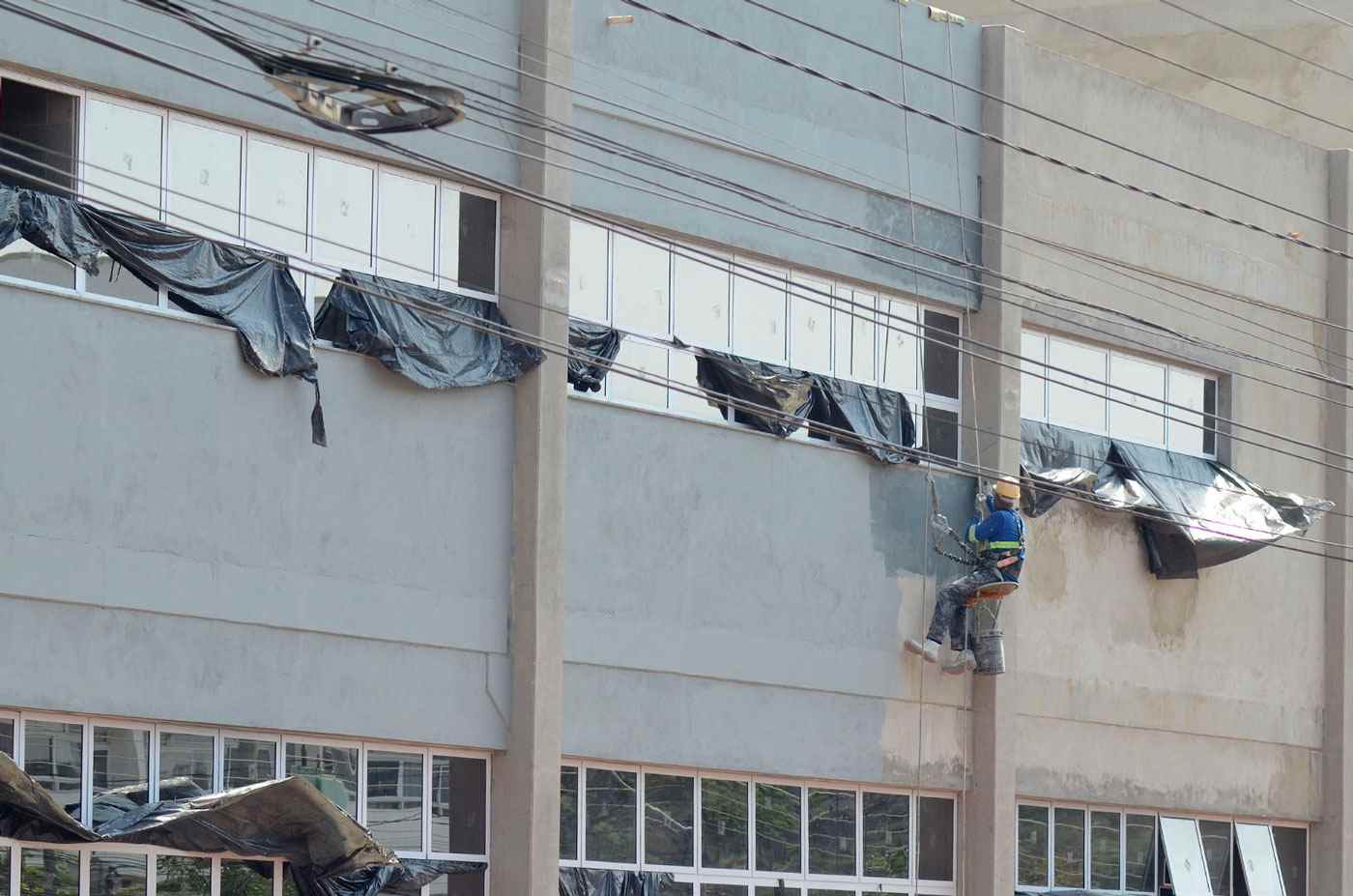 Trabalhador realizando pintura externa do novo hospital de Várzea Paulista, com estrutura em fase de acabamento.