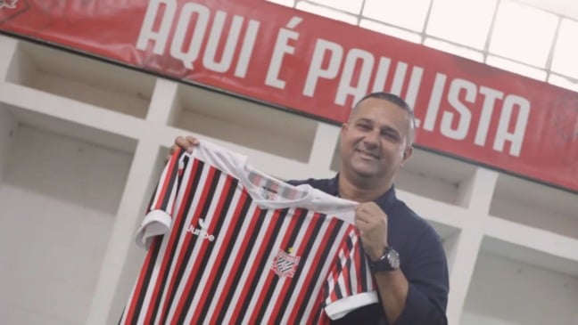 Novo técnico do Paulista FC, Raphael Pereira sorri enquanto segura a camisa tricolor do clube em sua apresentação no Estádio Dr. Jayme Cintra.