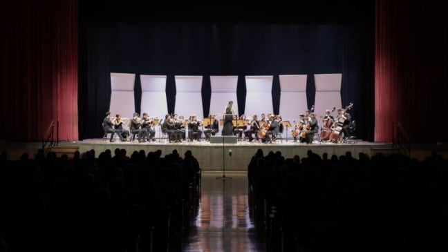 Orquestra Municipal de Jundiaí se apresenta no palco do Teatro Polytheama com regência da maestrina e músicos de cordas diante do público.