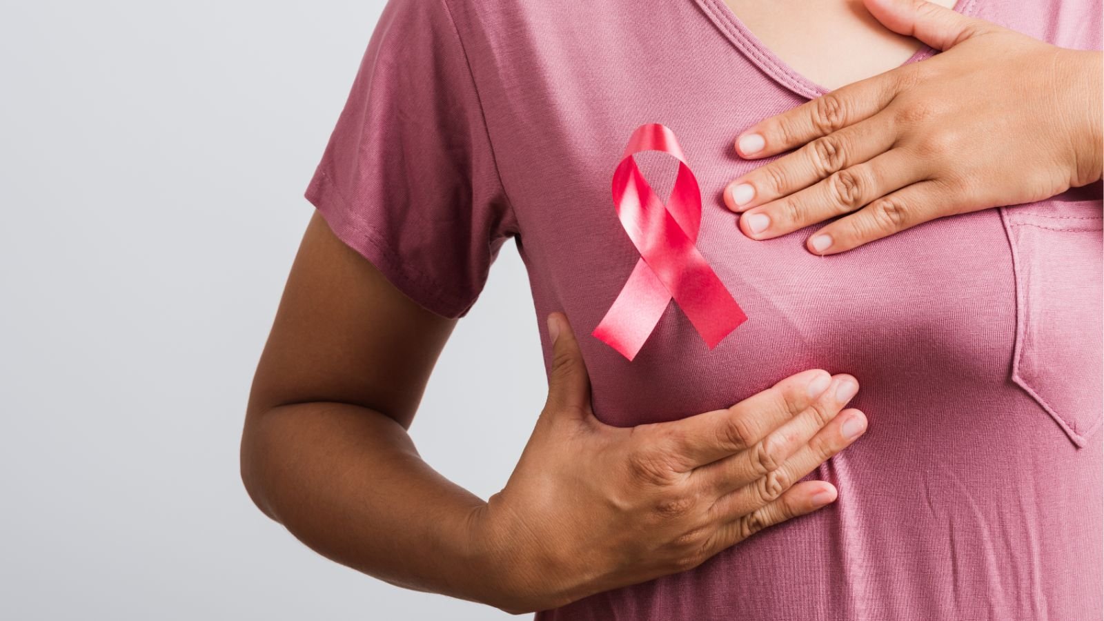 Mulher com laço rosa no peito faz autoexame das mamas em apoio à campanha Outubro Rosa.