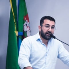 Vereador Faouaz Taha fala ao microfone na Câmara de Jundiaí, com bandeiras ao fundo. Vereador Faouaz Taha fala ao microfone na Câmara de Jundiaí, com bandeiras ao fundo.