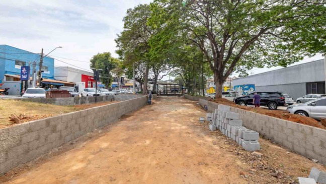 Obras de revitalização da Praça Joaquim Soares Lemos, em Jundiaí, com solo em preparação, blocos de concreto e árvores preservadas.
