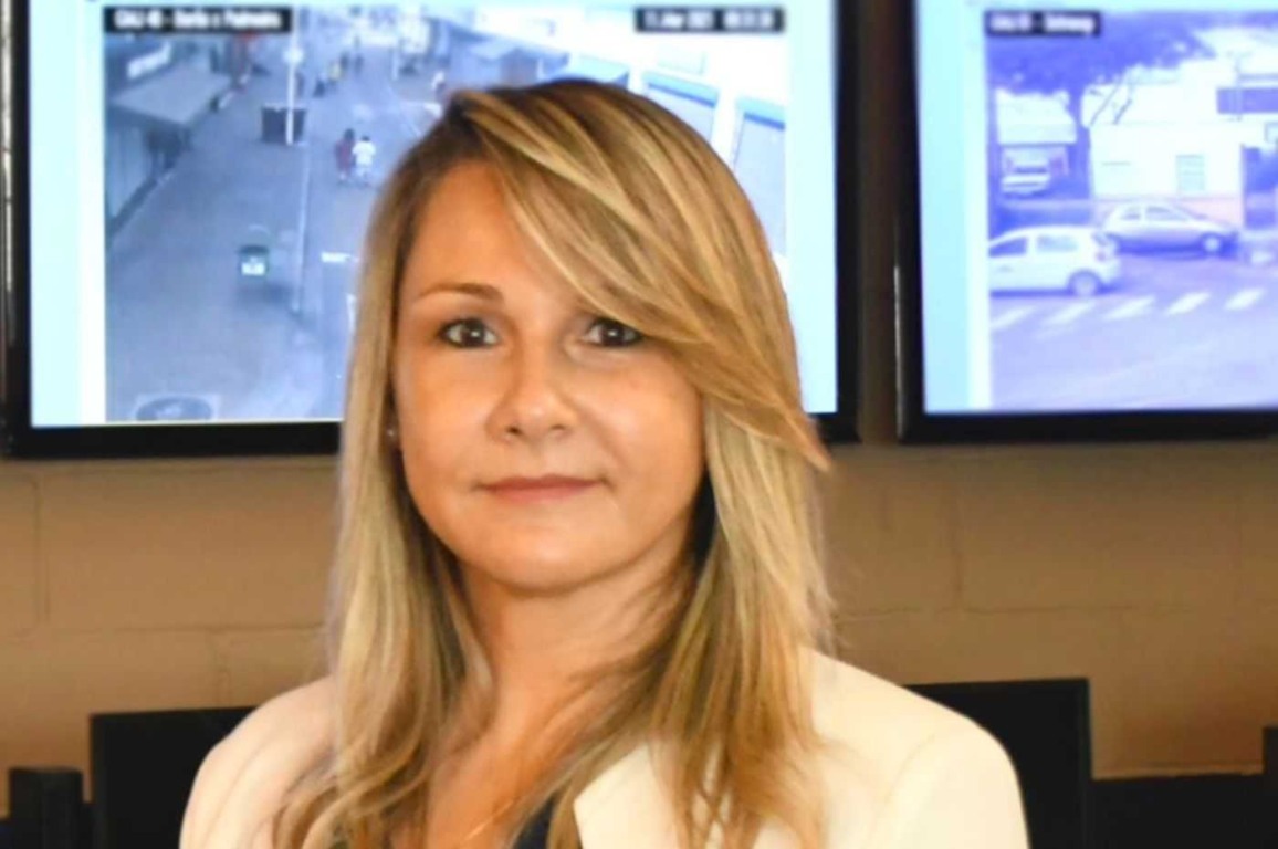 Carla Basson, loira, em ambiente de segurança, com monitores ao fundo, transmitindo profissionalismo e seriedade.