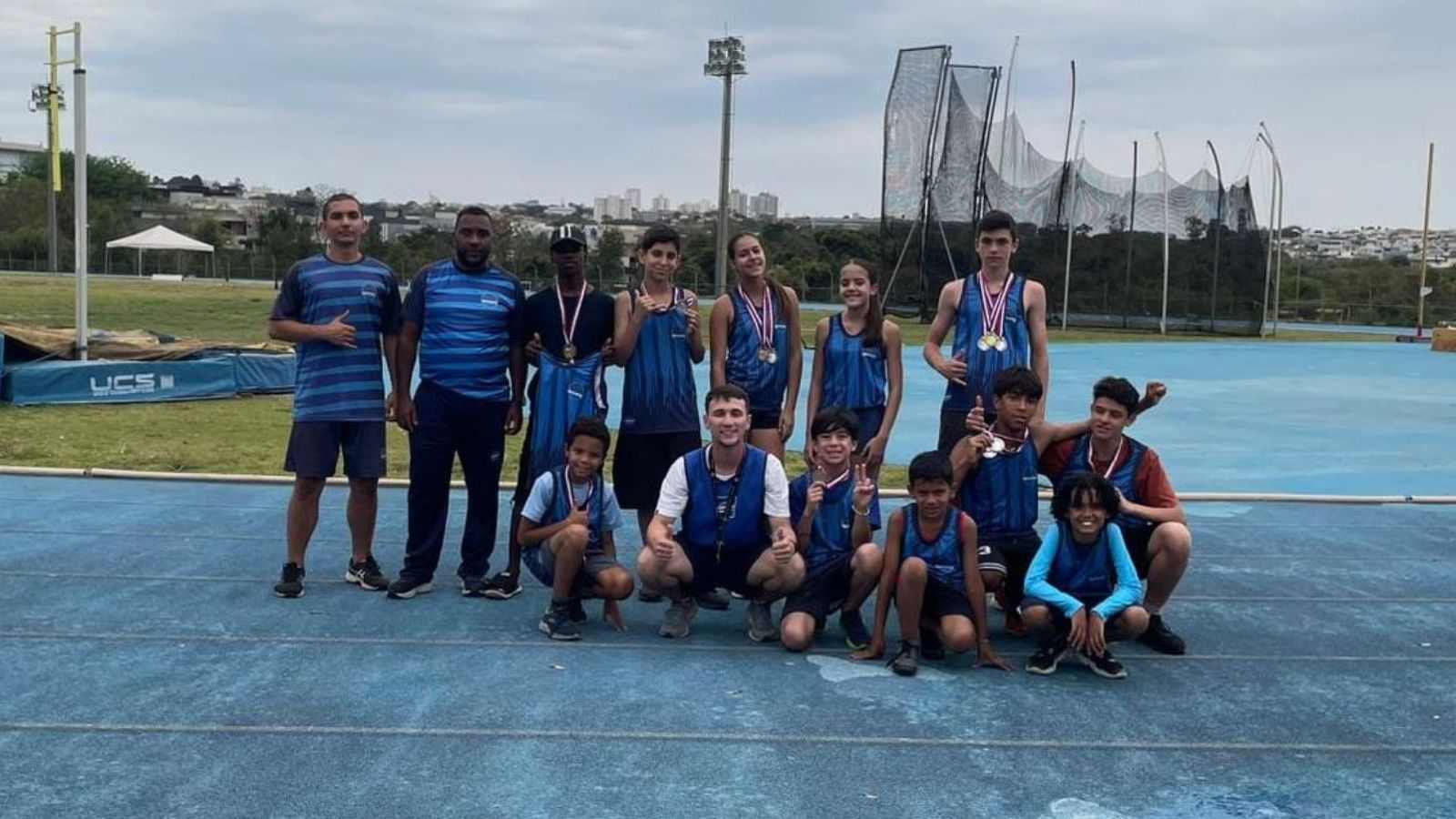 Equipe do Time Jundiaí com jovens atletas exibindo medalhas em pista de atletismo após conquistas no Pró-Atletismo em Campinas.