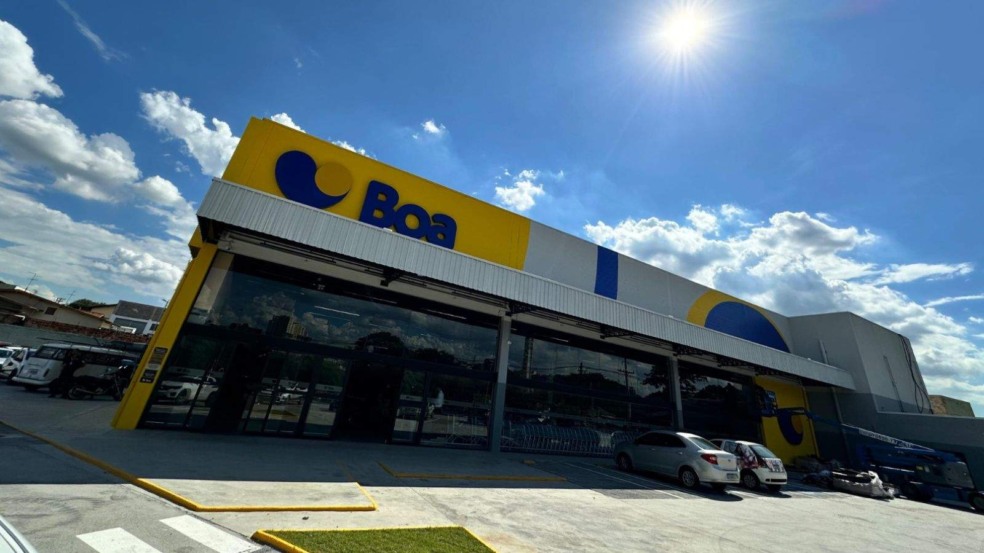 Fachada do Boa Supermercados em dia ensolarado, com logotipo azul sobre fundo amarelo e carros estacionados na entrada da unidade. Fachada do Boa Supermercados em dia ensolarado, com logotipo azul sobre fundo amarelo e carros estacionados na entrada da unidade.