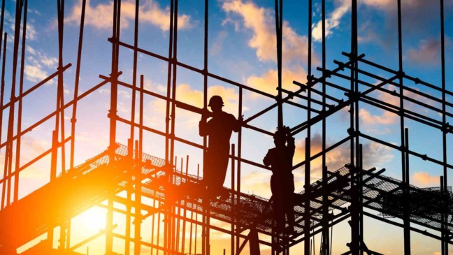 Dois operários da construção civil em uma estrutura de andaimes ao entardecer, representando vagas abertas pela Matec Engenharia em Jundiaí.