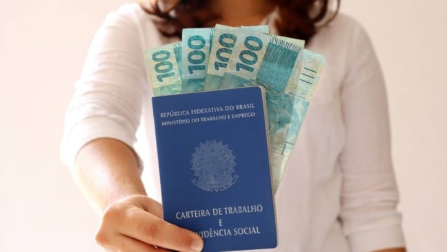 Carteira de Trabalho com cédulas de R$ 100, representando emprego e salário no Brasil.
