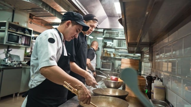 Cozinheiros preparando alimentos em uma cozinha profissional com ambiente industrial e utensílios de restaurante. Cozinheiros preparando alimentos em uma cozinha profissional com ambiente industrial e utensílios de restaurante.