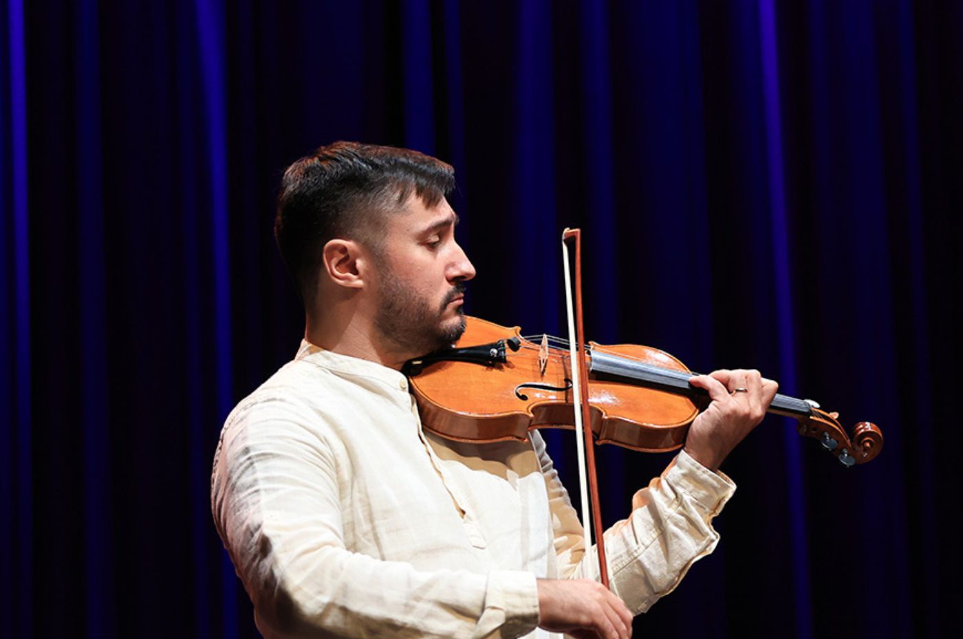 Violinista da Orquestra no Polytheama tocando concentrado no palco, com fundo azul escuro, em apresentação especial