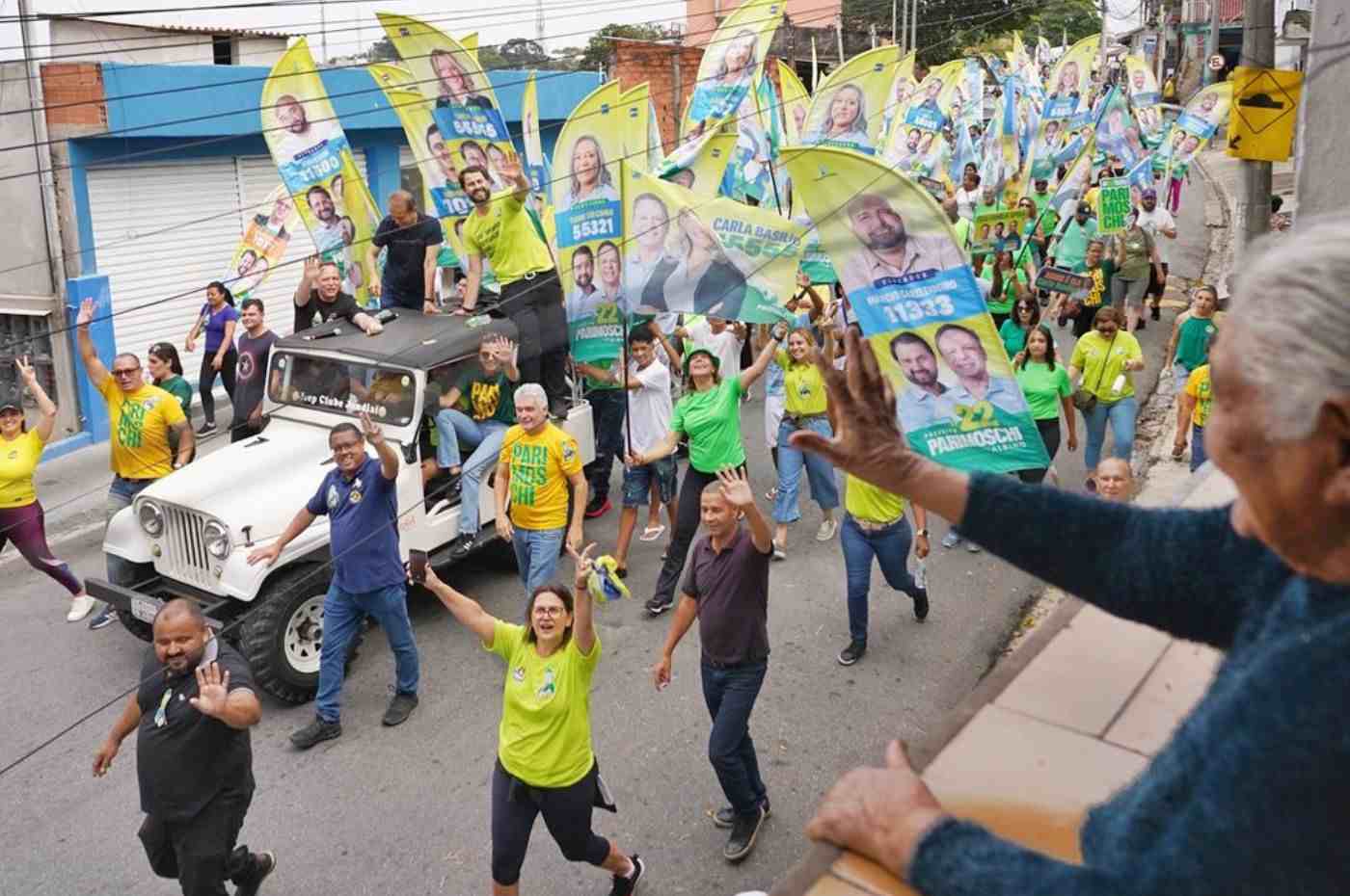 José Antônio Parimoschi em caminhada eleitoral pelo bairro São Camilo, Jundiaí, com apoiadores segurando bandeiras e cartazes de campanha.