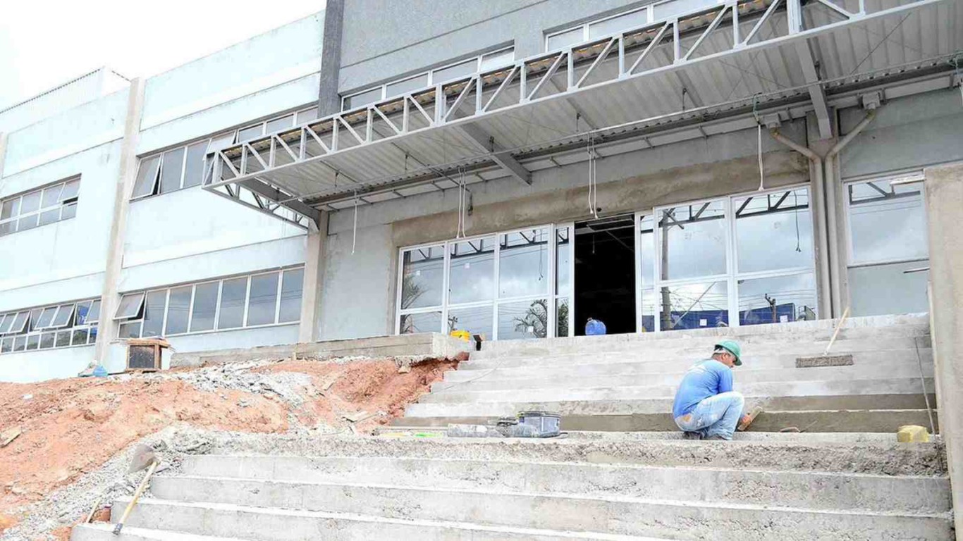 Fachada do Hospital de Várzea Paulista em construção, com trabalhador realizando acabamento nos degraus da entrada.