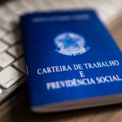 Carteira de Trabalho azul sobre um teclado branco, representando emprego e mercado de trabalho no Brasil.