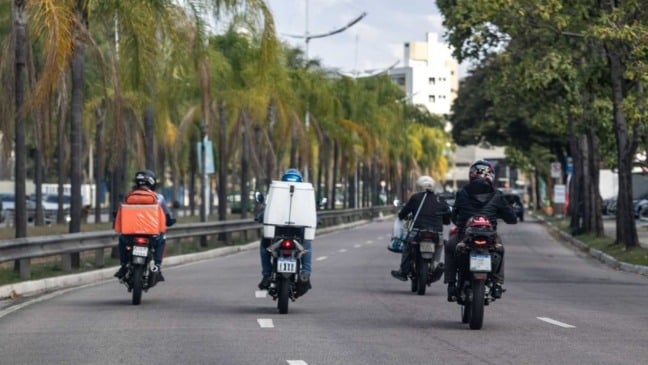 Entregadores de moto circulando por avenida arborizada em Jundiaí, com mochilas de delivery nas costas. Entregadores de moto circulando por avenida arborizada em Jundiaí, com mochilas de delivery nas costas.