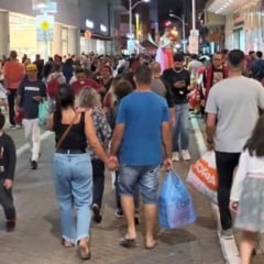 Rua comercial no Centro de Jundiaí lotada de pessoas caminhando e fazendo compras à noite, com vitrines iluminadas e consumidores carregando sacolas.