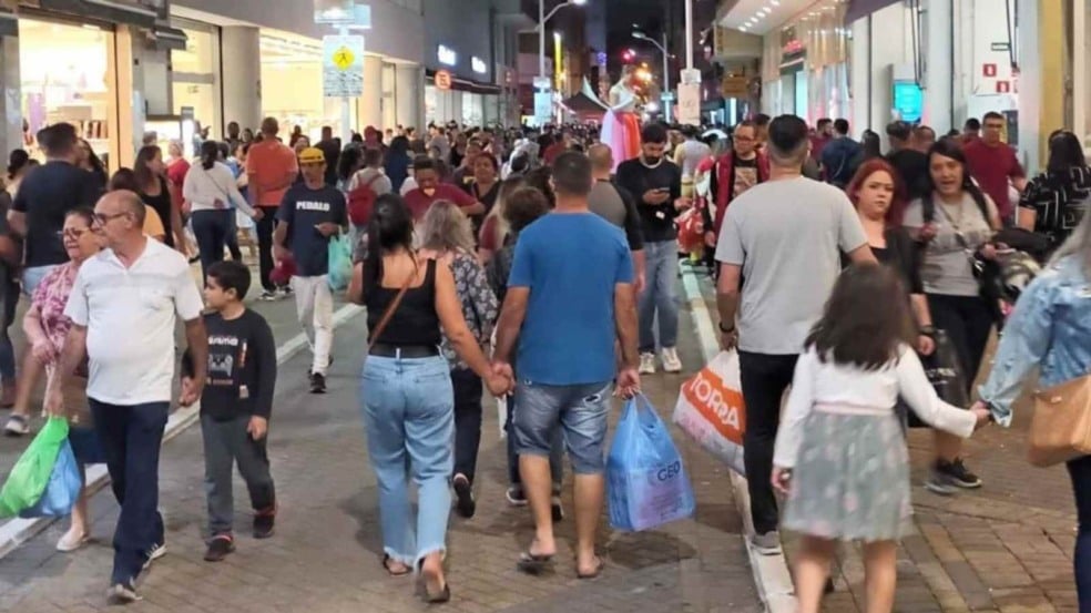 Rua comercial no Centro de Jundiaí lotada de pessoas caminhando e fazendo compras à noite, com vitrines iluminadas e consumidores carregando sacolas.