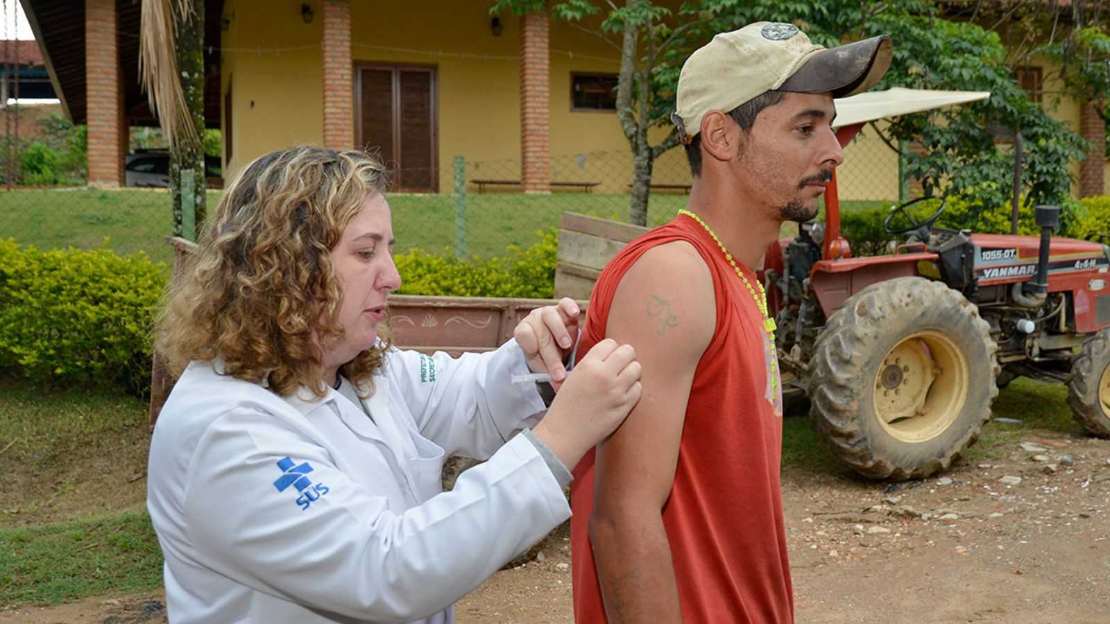 Profissional de saúde aplica vacina contra a febre amarela em morador de área rural durante campanha casa a casa em Jundiaí.