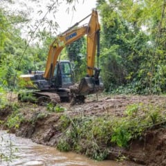 Escavadeira remove sedimentos nas margens de um rio cercado por vegetação, durante operação de desassoreamento em Jundiaí.