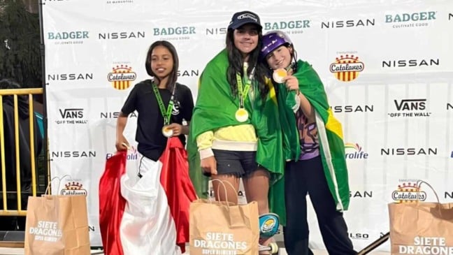 Alice Rizetto à esquerda segurando sua medalha e enrolada na bandeira do Brasil durante o pódio da competição.