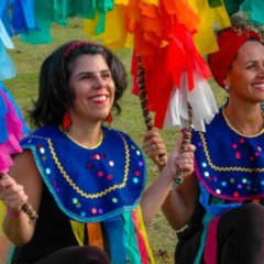 Aline Longui e Josiane Gomes, vestidas com trajes coloridos e segurando bastões decorados com fitas, participam de atividade do projeto Andanças do Ser-Tão Brincante em área verde de Jundiaí.
