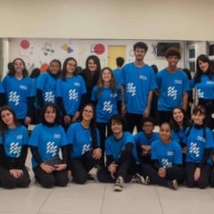 Coral juvenil das Oficinas Culturais reunido em sala de ensaio, com cerca de 25 jovens usando camisetas azuis e posando para foto em grupo.